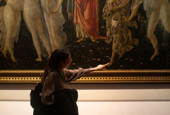 Visitor reaching toward a large Renaissance painting of dancing figures in a gilded frame