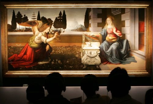 Visitors silhouetted in front of a Renaissance Annunciation painting in a gallery