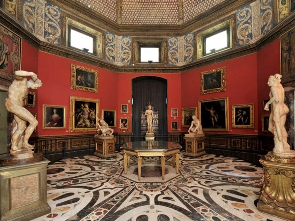 Octagonal Tribuna room of the Uffizi with red walls, framed paintings, statues and an inlaid marble floor