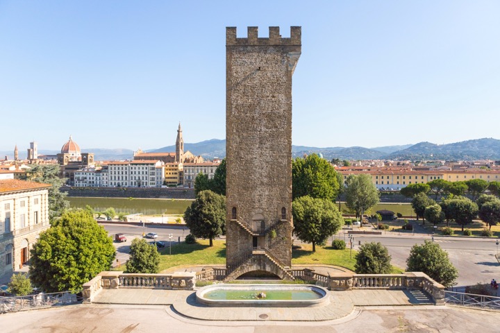 Crenellated stone tower rising over a fountain basin, with the Arno and Florence's skyline in the distance