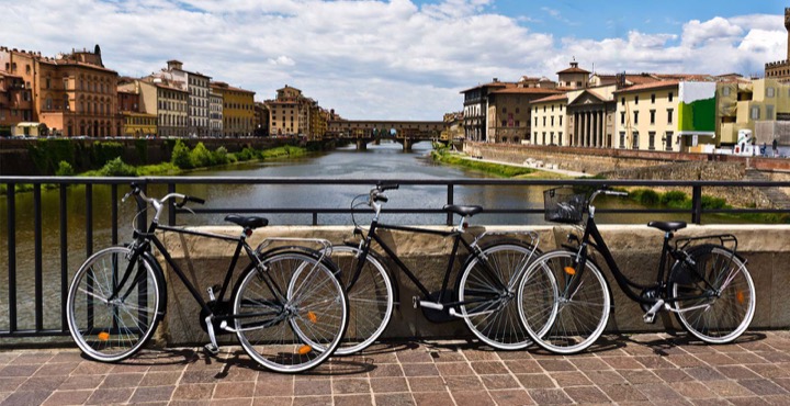 Three bicycles leaning on a parapet beside the Arno, with the Ponte Vecchio in the background