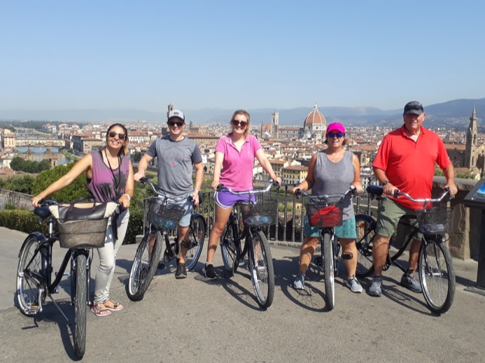 Group of five cyclists posing with bikes at a viewpoint, with the Duomo and the city behind