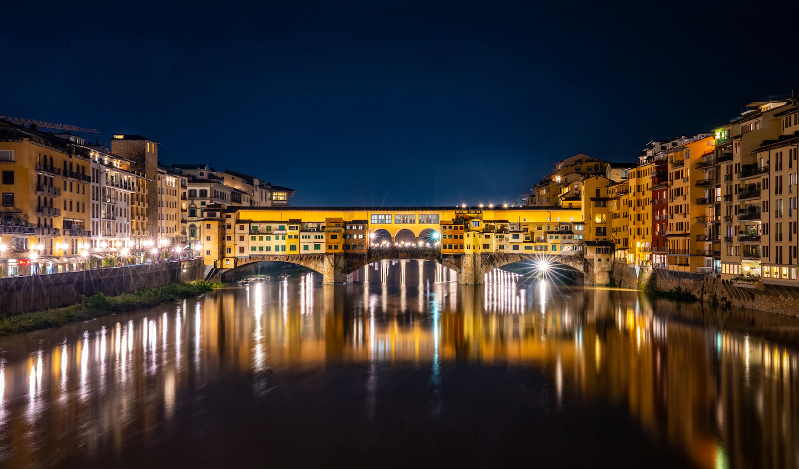 Ponte Vecchio lit up at night with golden reflections on the Arno
