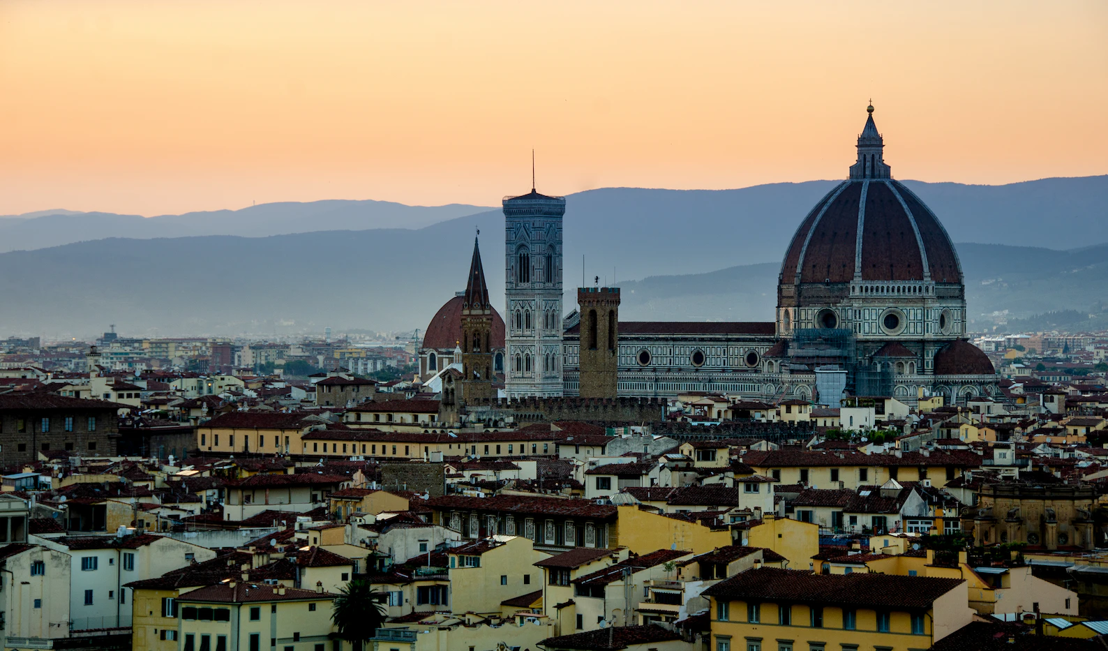 Florence cathedral dome and bell tower silhouetted against an orange sunset sky
