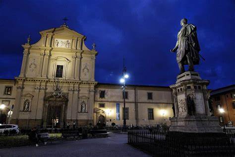 Piazza San Marco in Florence at dusk with the church facade and an equestrian-style monument lit up