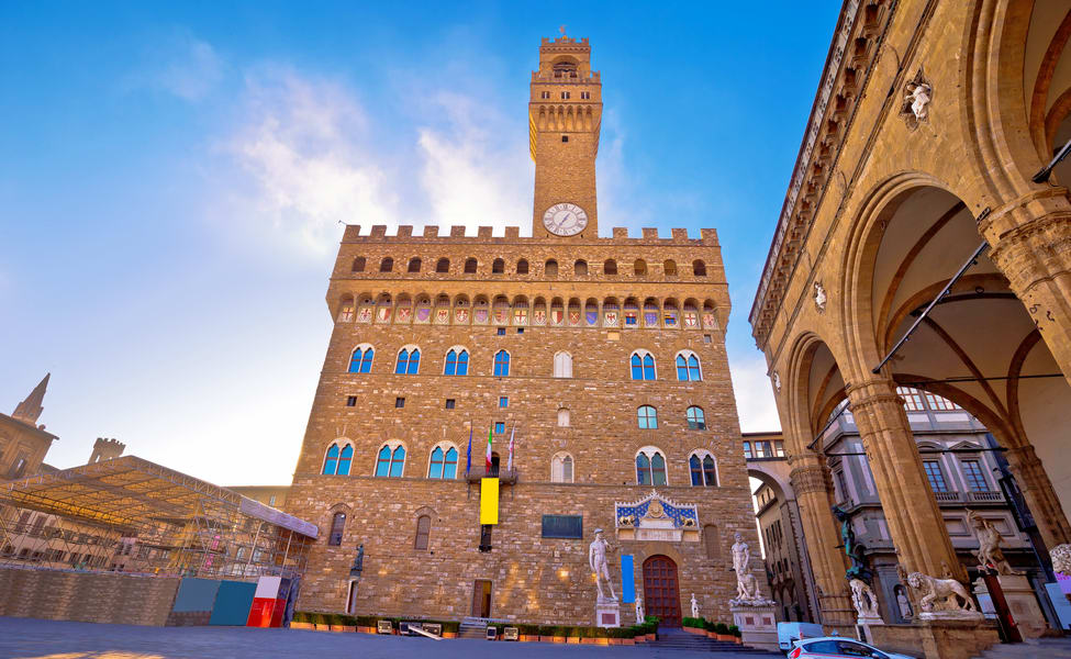 Palazzo Vecchio with its crenellated tower and clock, beside the arches of a loggia in Florence