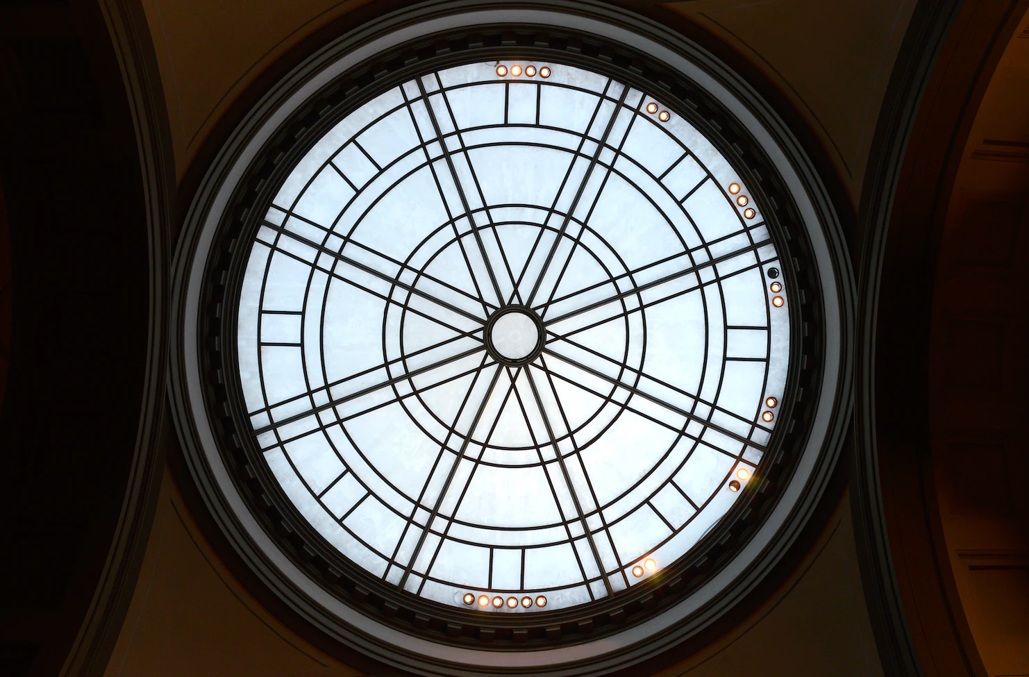 Circular glass skylight with iron spokes seen from below inside a museum