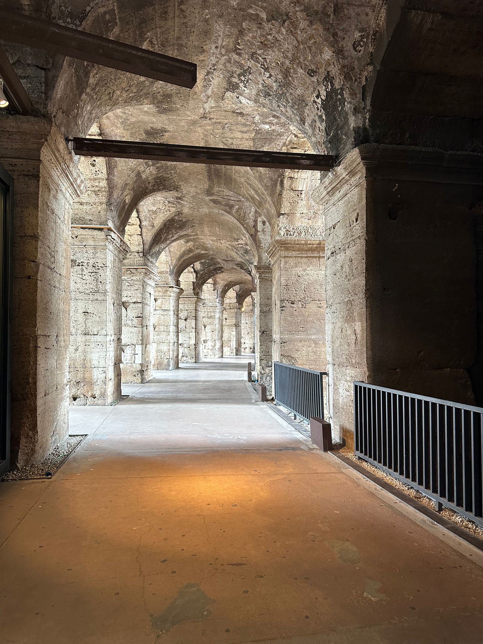 Vaulted stone passageway inside the Colosseum with metal railings and warm light on the floor