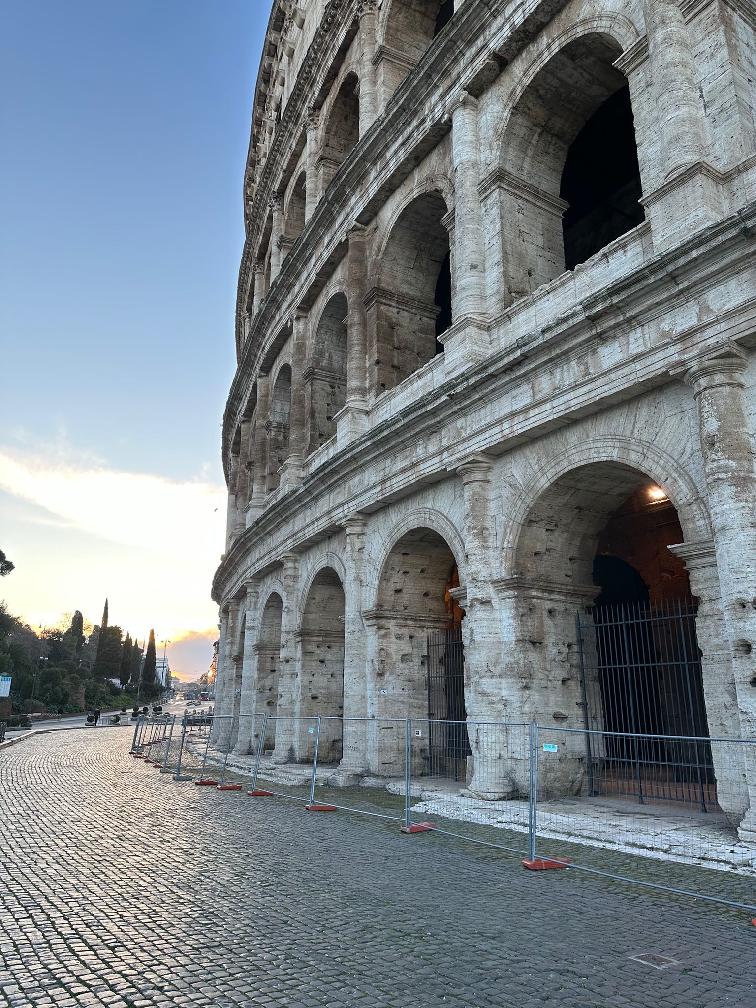 Colosseum arches in soft morning light beside a cobbled road and temporary fencing