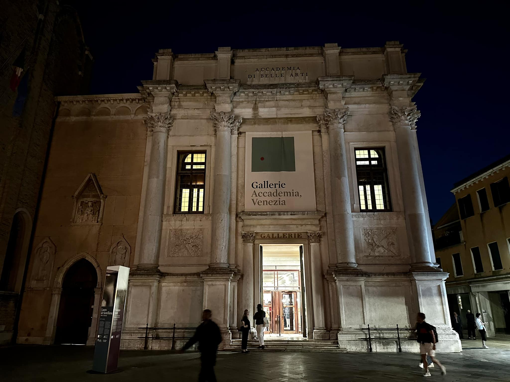 Floodlit neoclassical facade of the Gallerie dell'Accademia in Venice at night, with visitors outside
