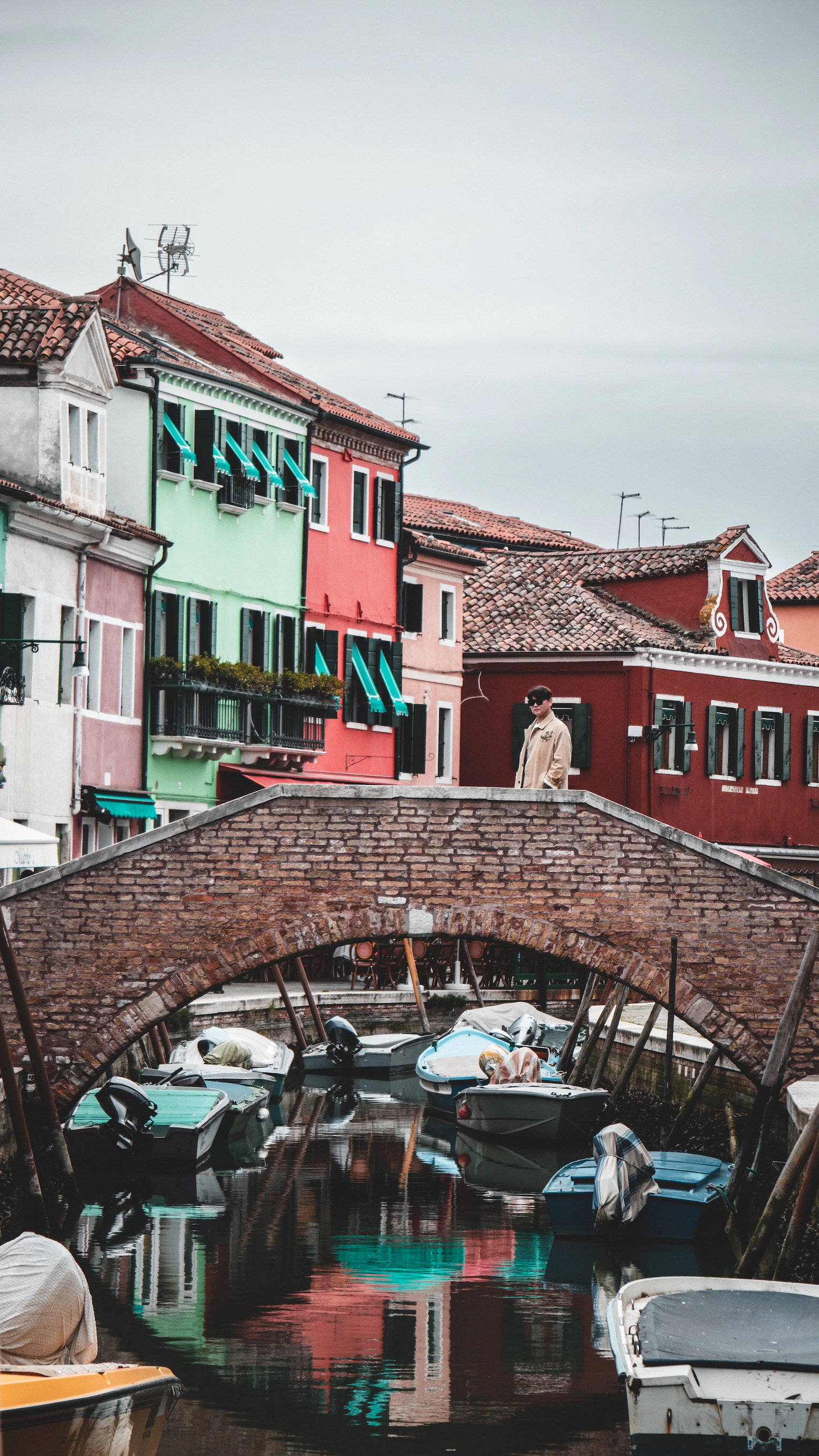 Brick bridge over a canal lined with moored boats and brightly painted houses in the lagoon