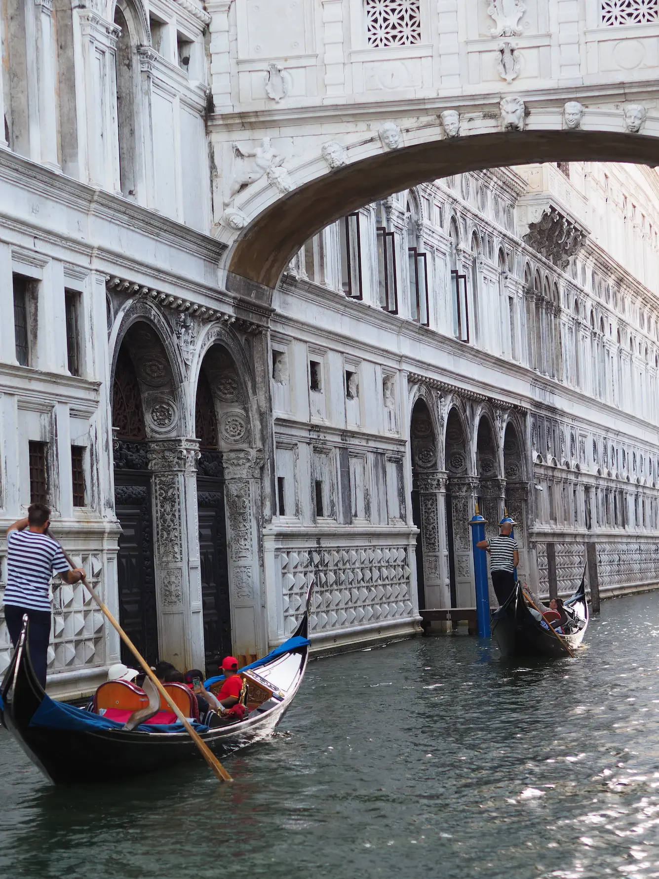 Gondolas passing beneath the Bridge of Sighs beside the white walls of the Doge's Palace