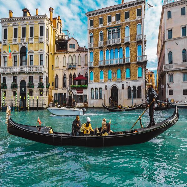 A gondola with passengers and a gondolier gliding along the turquoise Grand Canal past colourful palazzi
