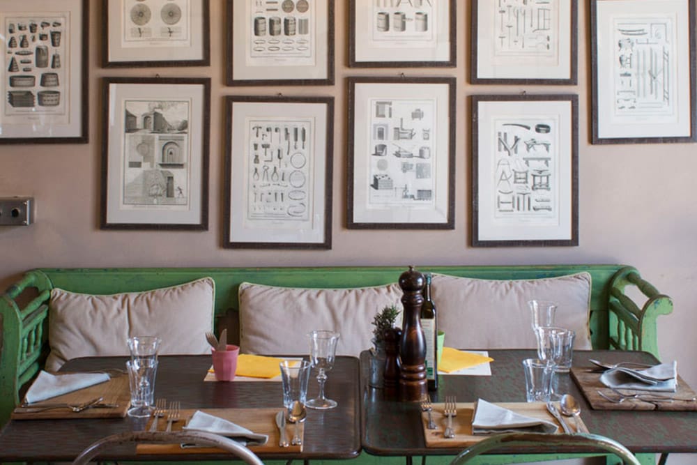 Rustic farm restaurant corner with a green bench, framed botanical prints and set tables