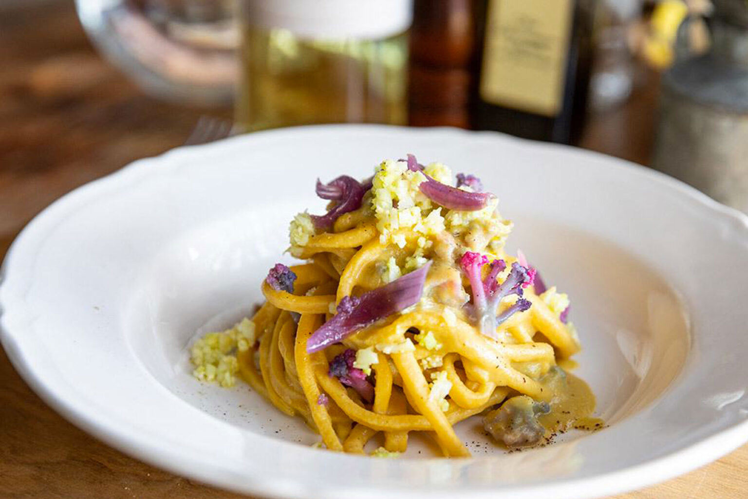 Plate of fresh egg pasta with cauliflower and purple vegetable garnish on a white dish