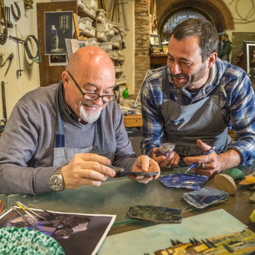 Two smiling artisans working on semi-precious stone inlays at a bench in a Florentine workshop