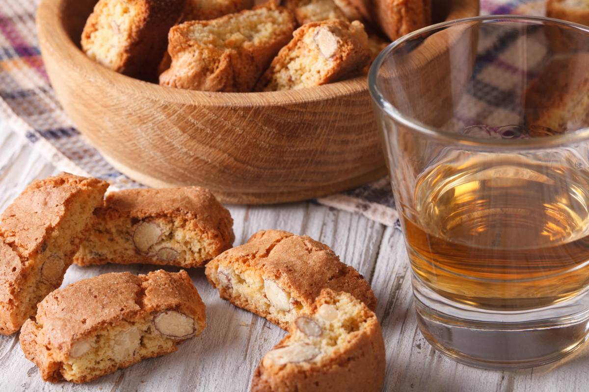 Almond cantucci biscuits in a wooden bowl beside a glass of amber dessert wine