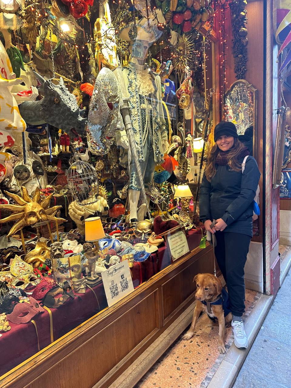 Visitor with a dog outside a Venetian shop window full of masks and costumes