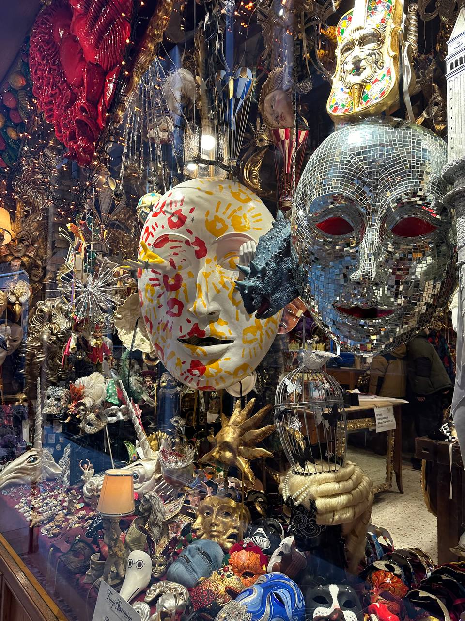 Shop window display with a mirrored mosaic mask, a painted white mask and golden hands