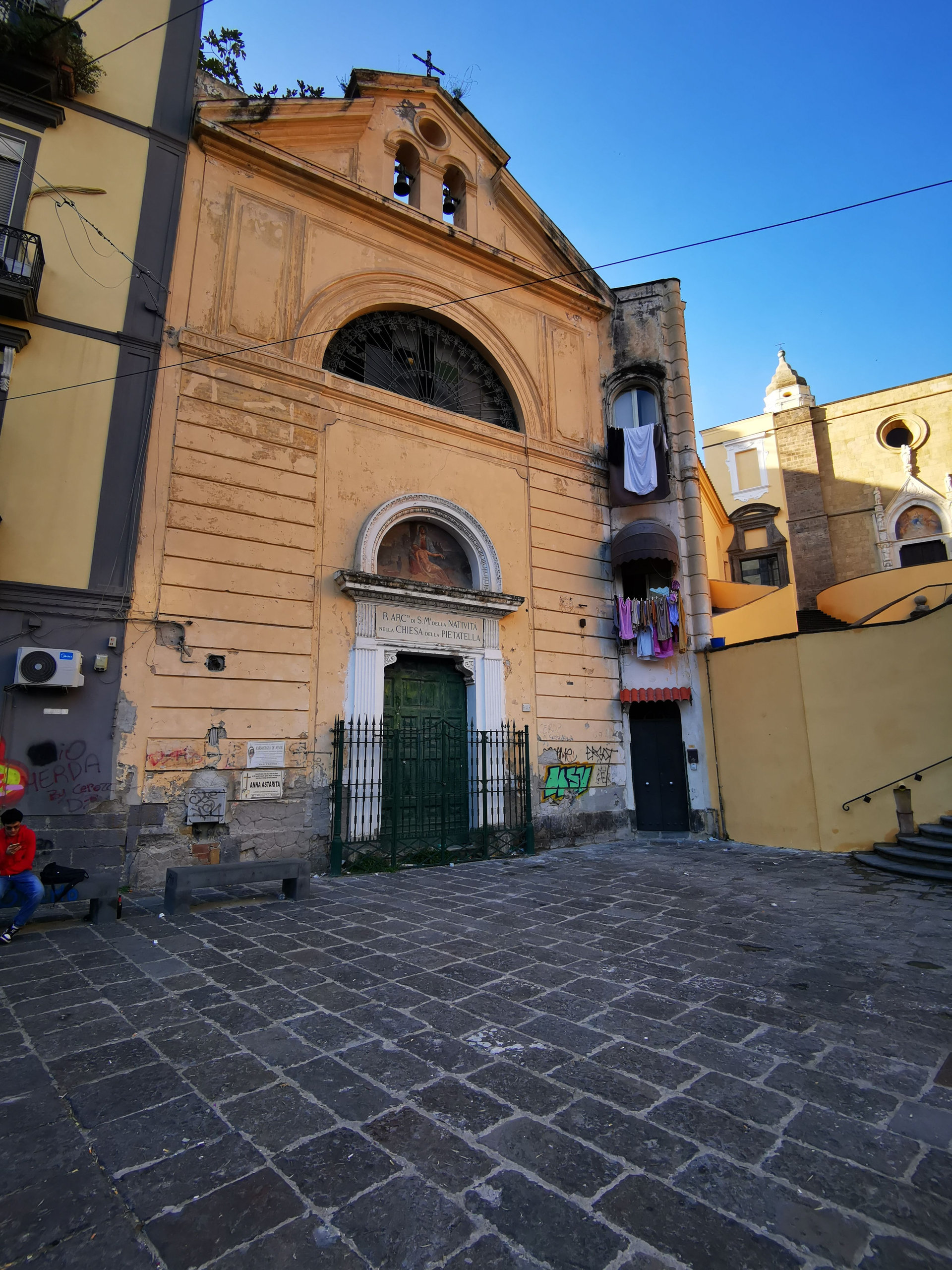 Weathered ochre church facade with a green door on a cobbled square in Naples