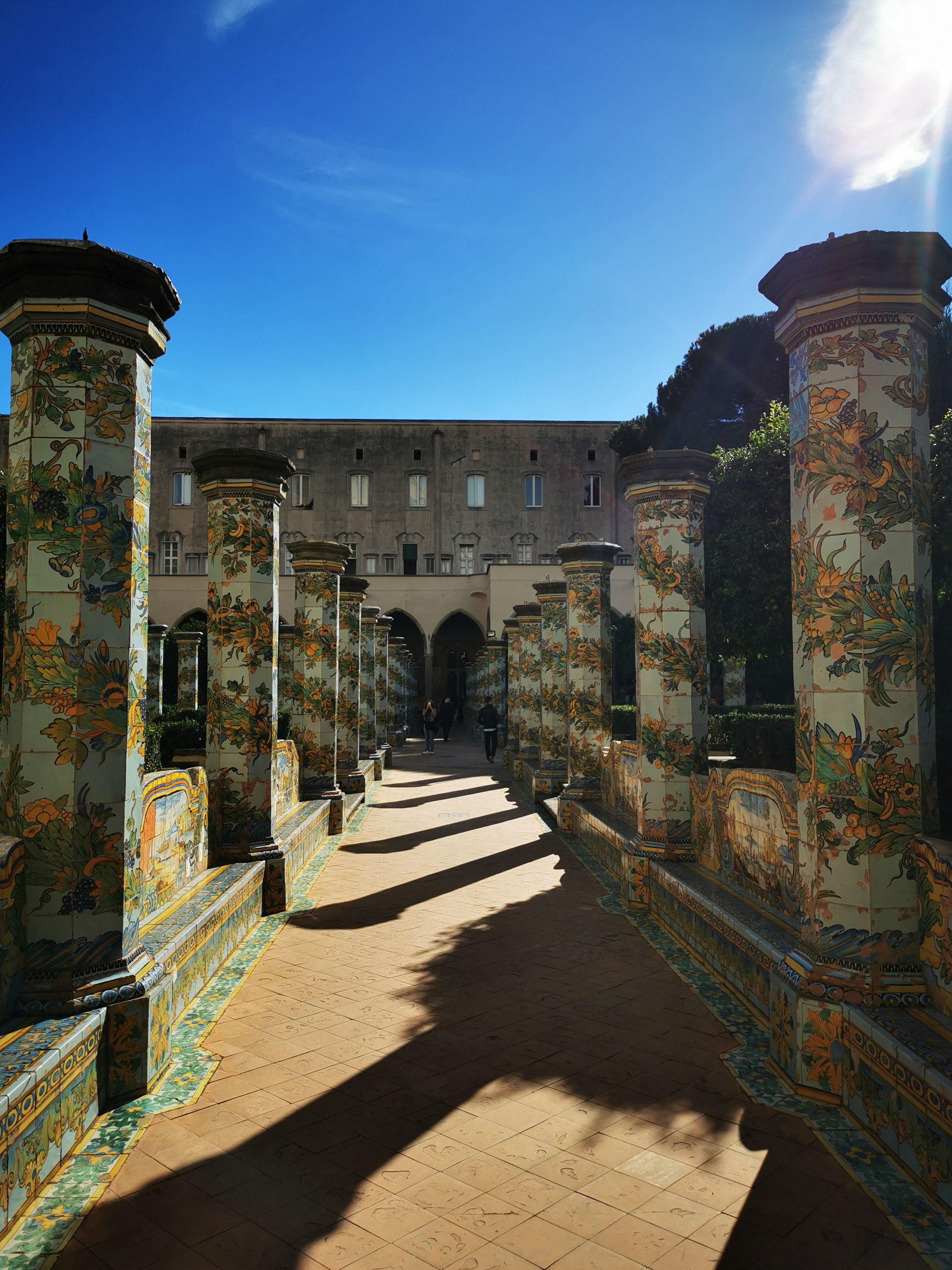 Sunlit cloister walkway lined with columns painted in colourful floral majolica