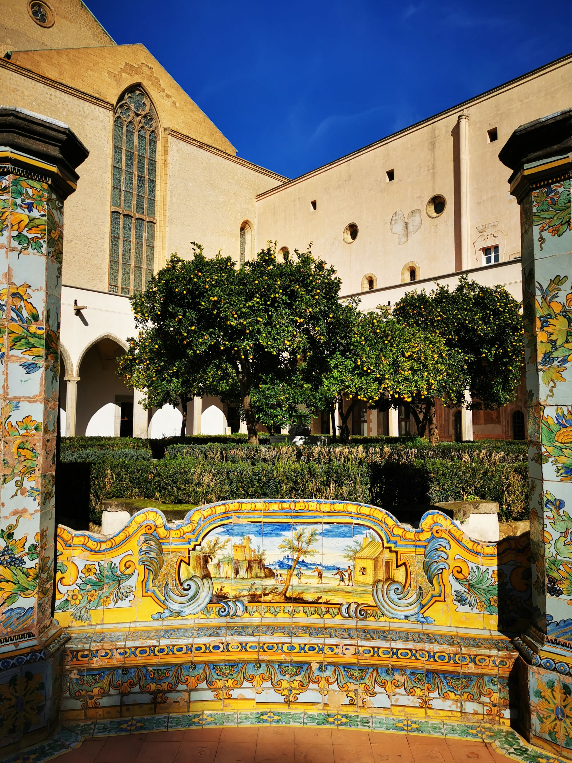 Hand-painted majolica bench and orange trees in a cloister garden beneath a church wall