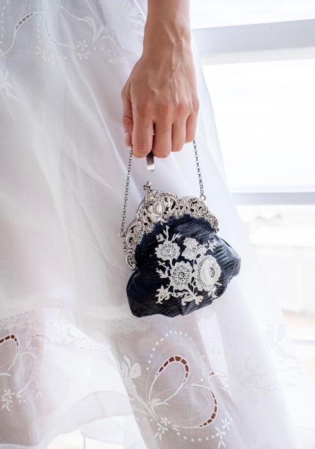 Hand holding a small navy evening bag with a silver clasp and white lace flowers