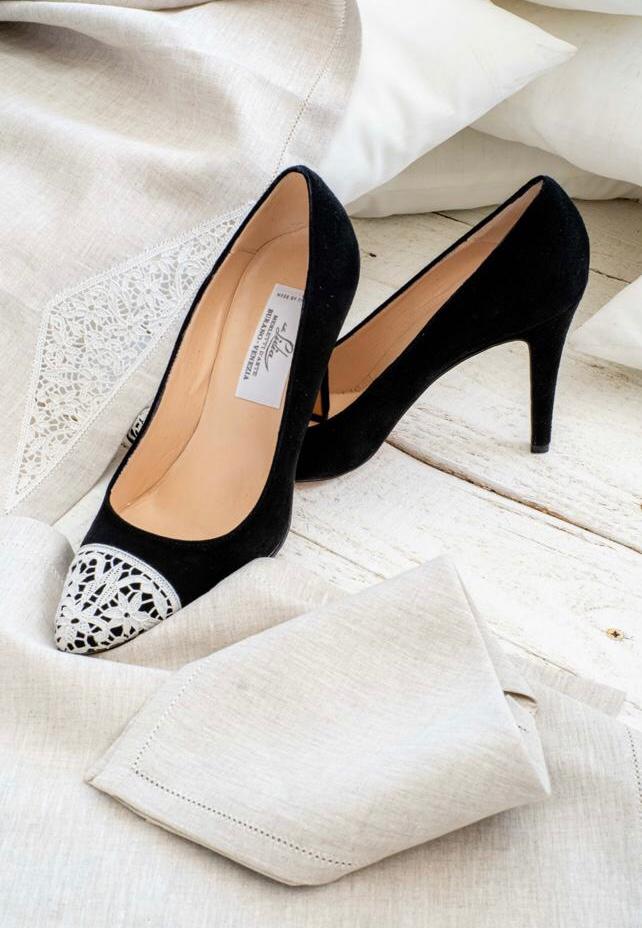 Black suede high heels with lace toe caps resting on linen cloth
