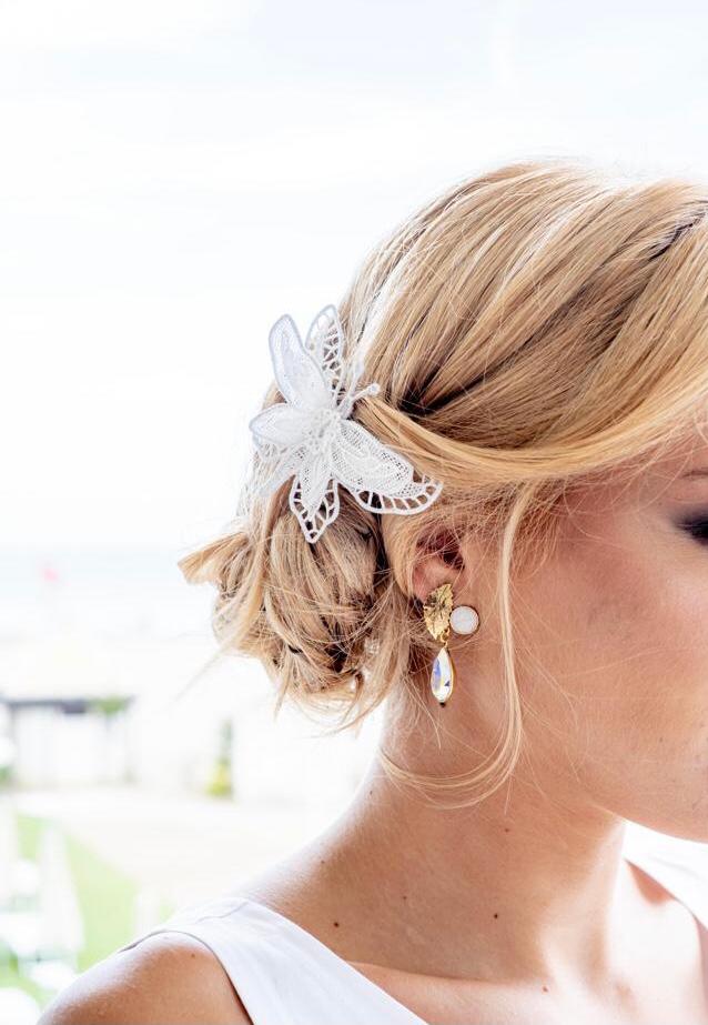 Woman with an upswept hairstyle wearing a white lace hair flower and gold drop earrings