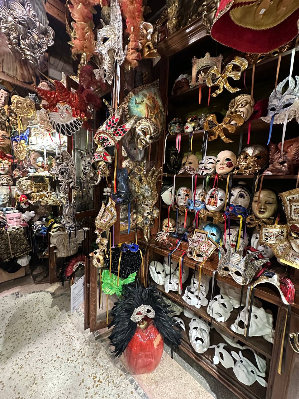 Shelves and walls crowded with ornate Venetian carnival masks and feathers in a traditional shop