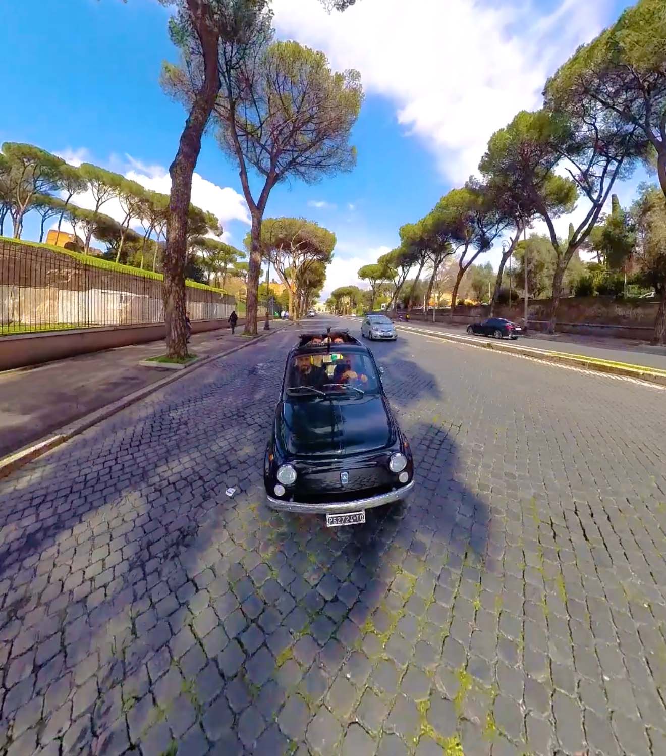 Vintage black Fiat 500 driving on a cobbled road lined with umbrella pines in Rome