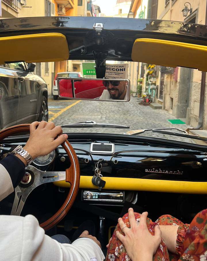 Driver's view from inside a vintage convertible with a wooden steering wheel and yellow dashboard trim