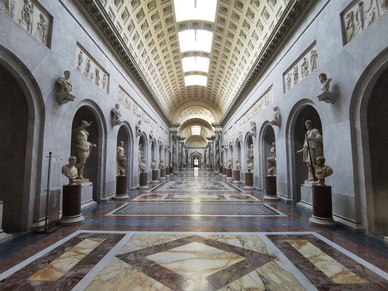 Long vaulted gallery in the Vatican Museums with statues in niches and a marble mosaic floor