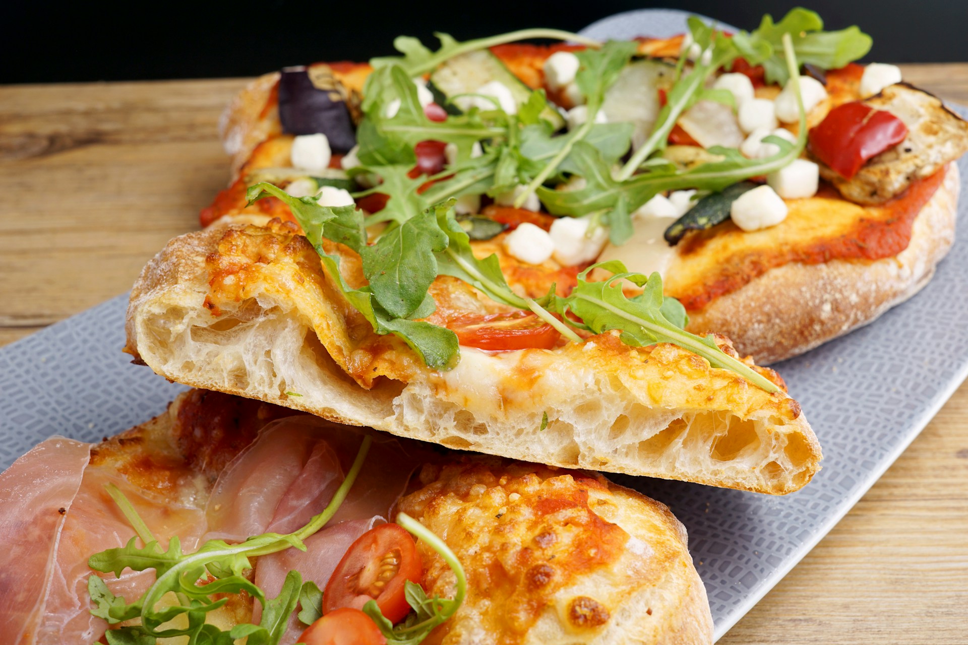Slices of pizza topped with rocket, mozzarella, vegetables and cured ham on a tray