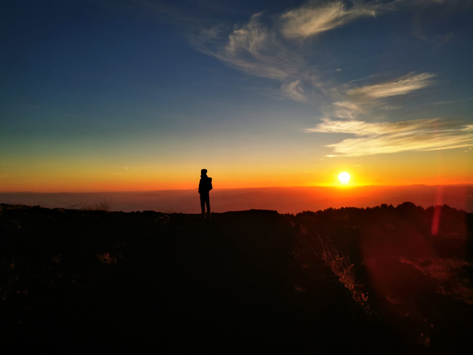 Silhouetted traveller watching the sun set over a glowing orange horizon from the volcano