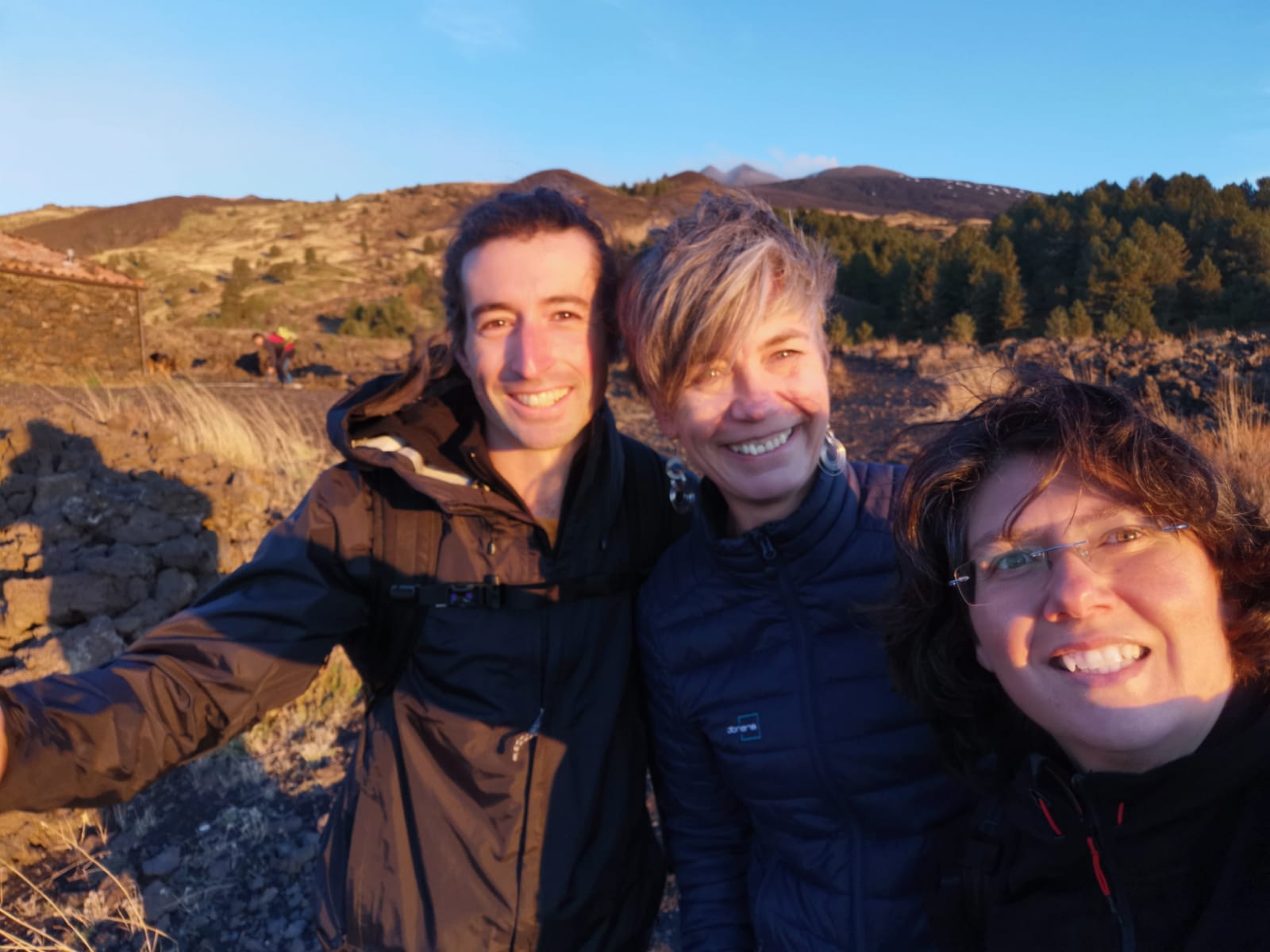 Three smiling travellers taking a selfie in warm evening light on the slopes of Etna