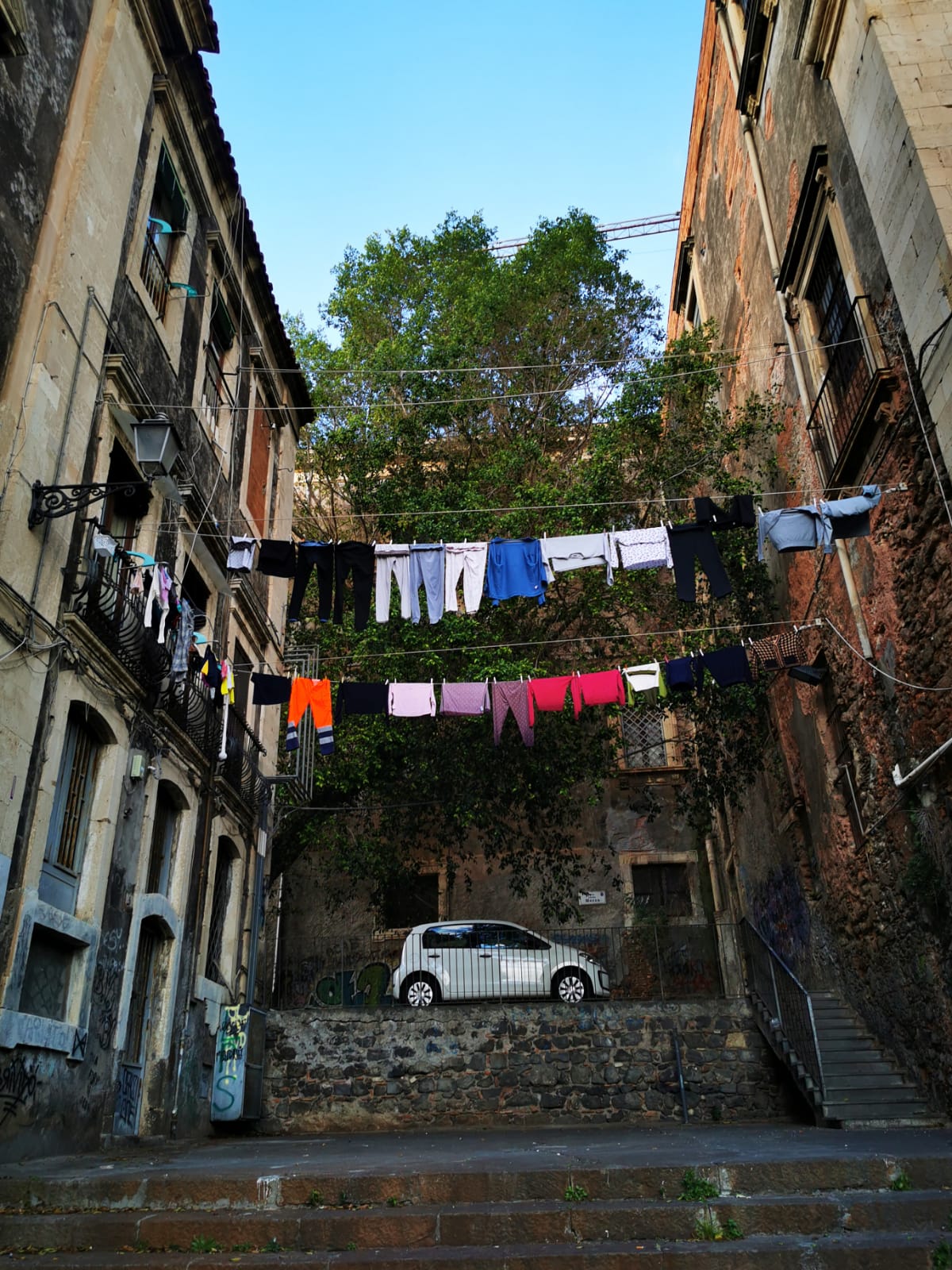 Washing hung on lines across a narrow lane between old stone houses, with a stepped street below