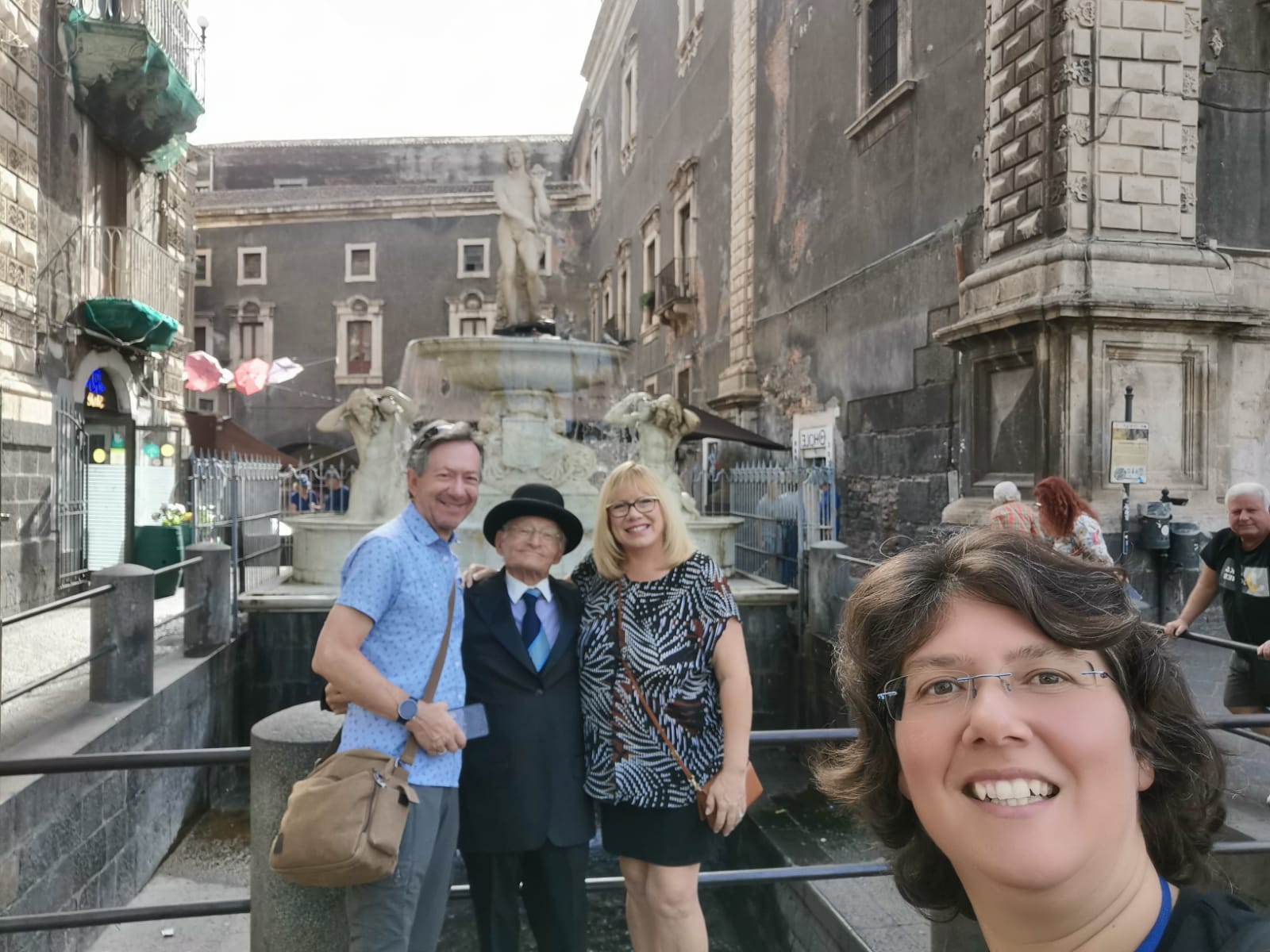 Travellers and a guide posing in front of a stone fountain on a Catania street