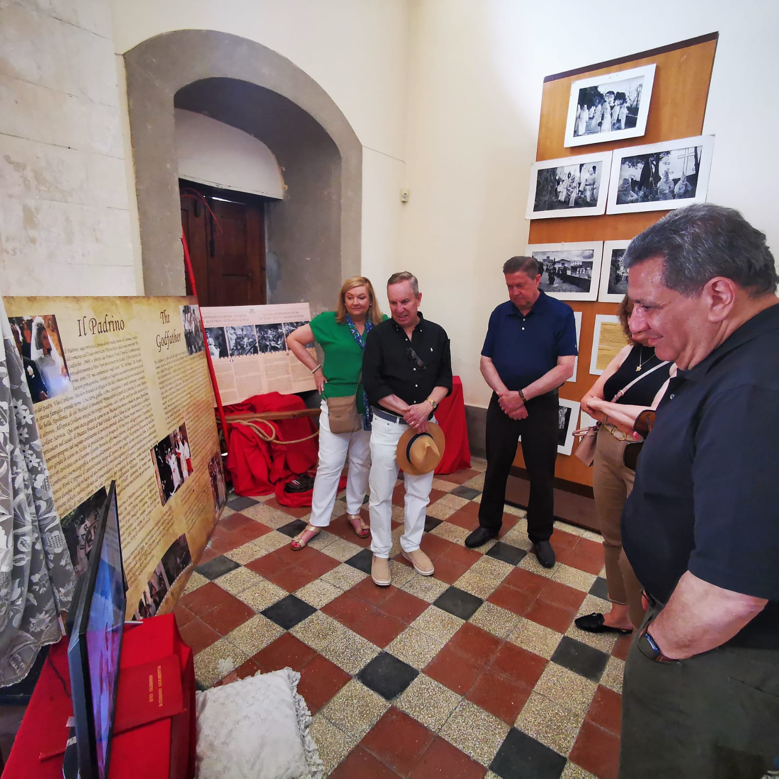 Travellers looking at Godfather photographs and memorabilia in a small exhibition room with a chequered floor