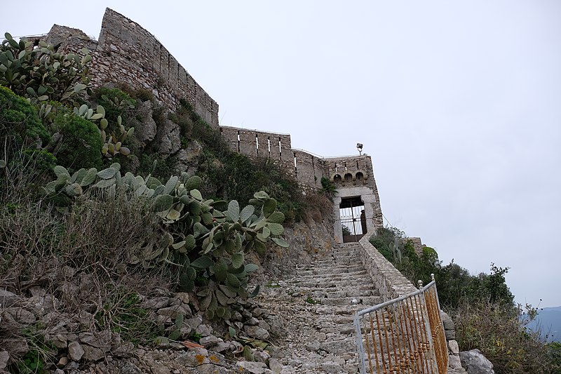 Stone steps climbing to a hilltop fortress gate framed by prickly pear cactus
