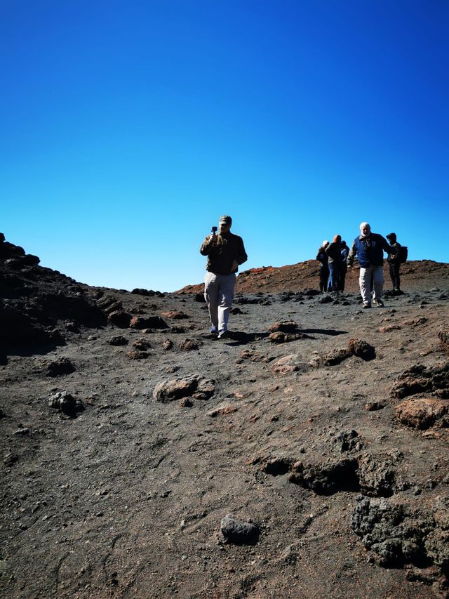 Group of walkers crossing a barren field of dark volcanic rock under a deep blue sky