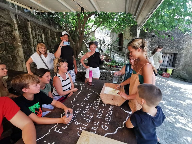 Group gathered around a wooden table in a courtyard for a pasta-making class