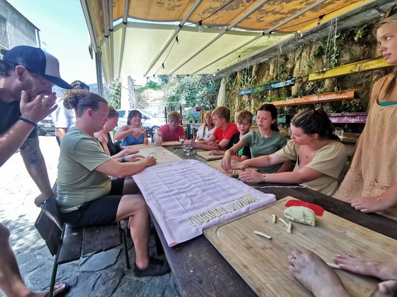 Participants seated at long tables under an awning, shaping pasta by hand