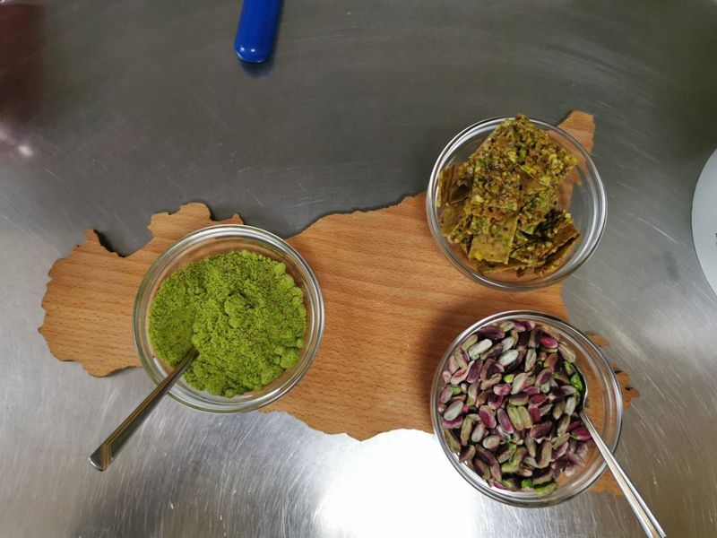 Bowls of pistachio powder, crushed brittle and whole pistachios on a Sicily-shaped wooden board