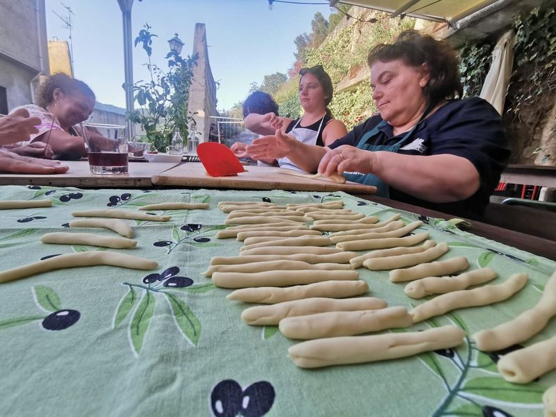 Rows of hand-rolled pasta strands on an olive-print tablecloth as women work the dough