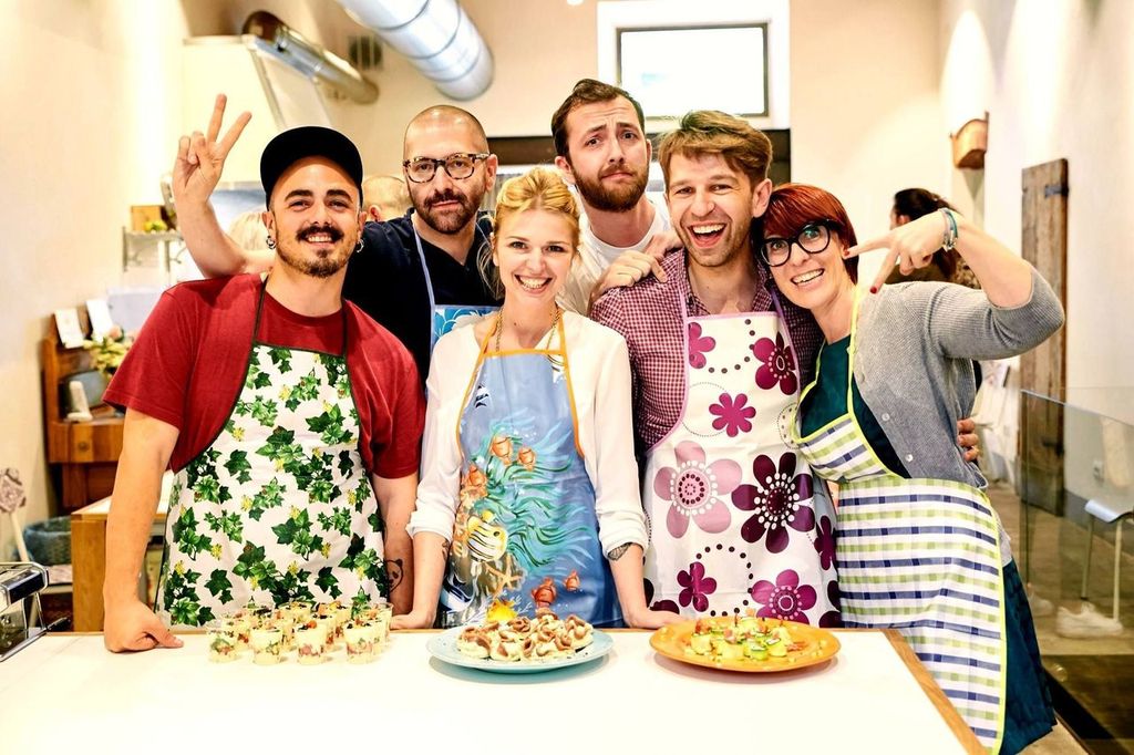 Group of smiling cooking-class participants in aprons posing behind a counter with plated dishes