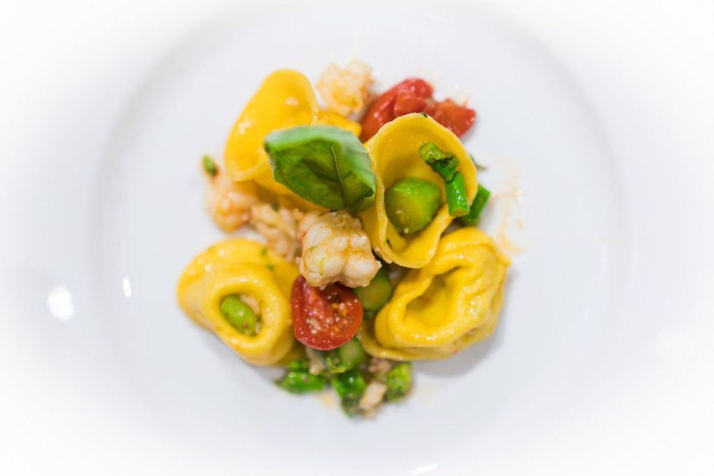 Plate of yellow tortelli with prawns, cherry tomatoes, green vegetables and basil