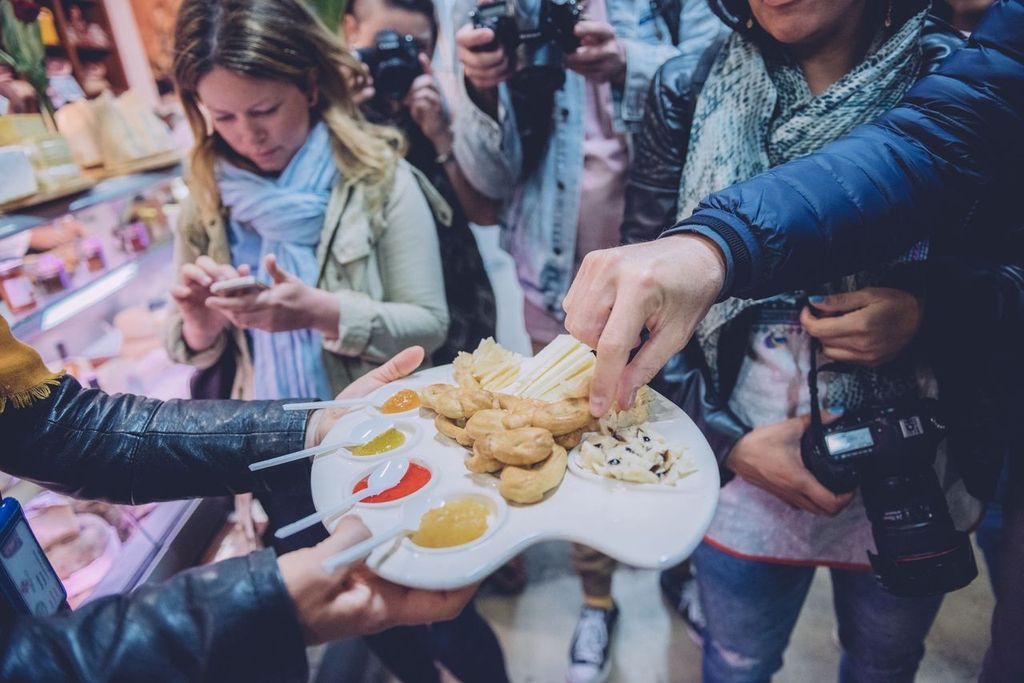 Visitors sampling cheeses and honey from a tasting platter at a food market