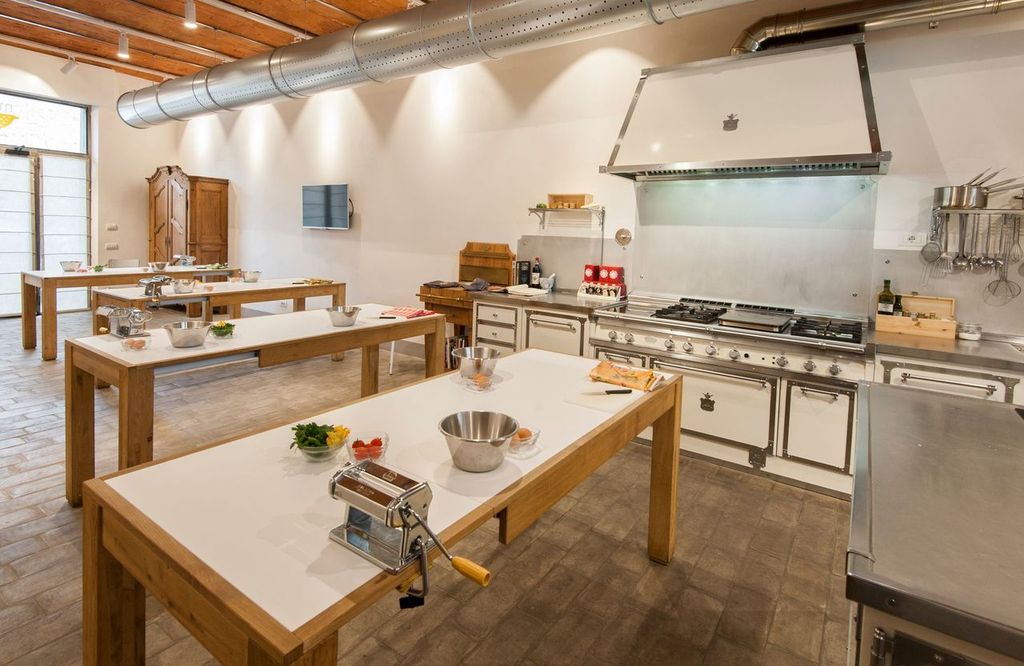 Bright cooking-class kitchen with long wooden worktables, a pasta machine and a professional stove