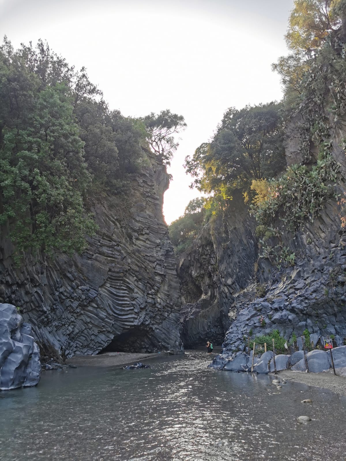Narrow Alcantara Gorge with walls of layered basalt rising above a shallow stream